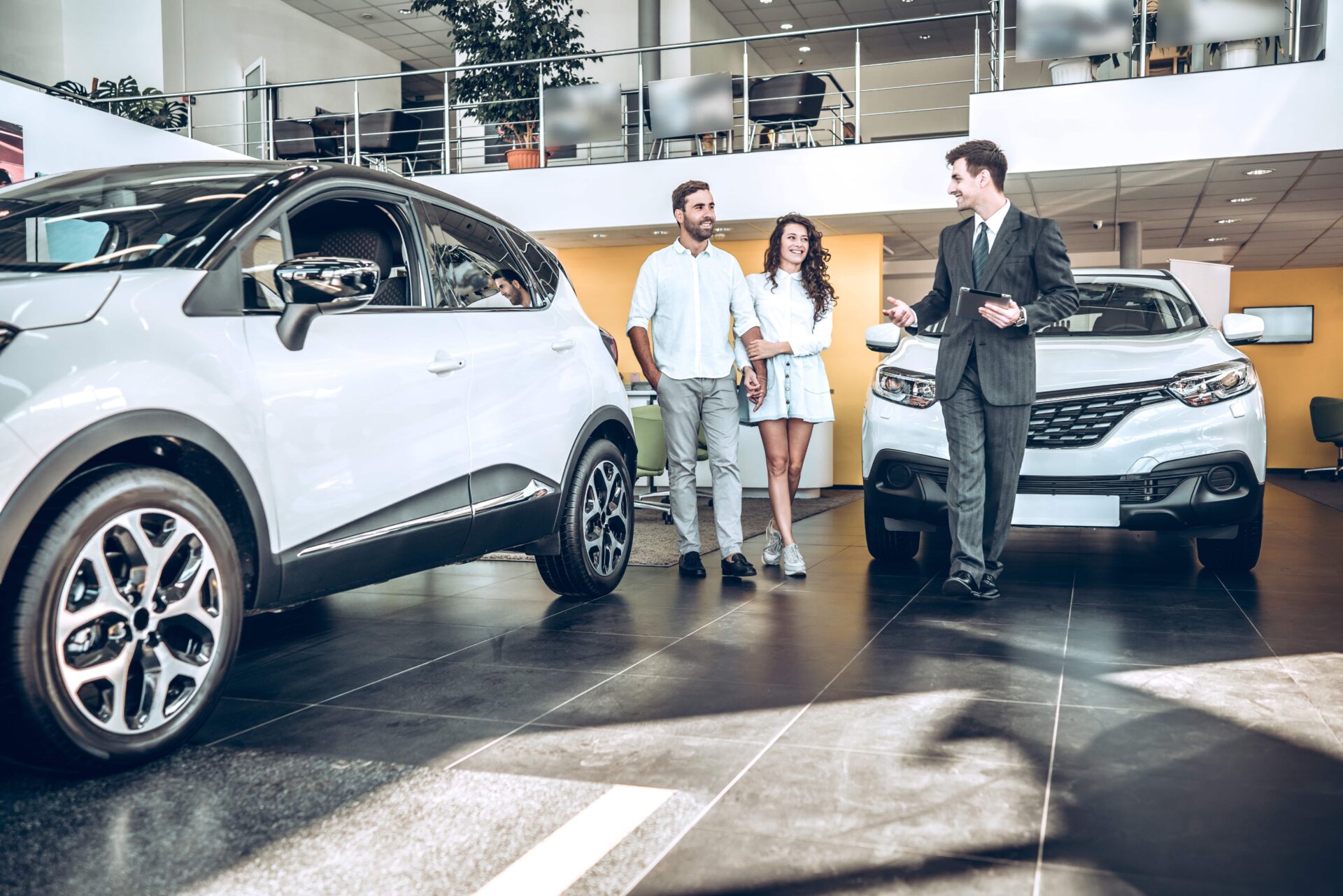 Sales manager helping young couple to choose a new car in modern car showroom.